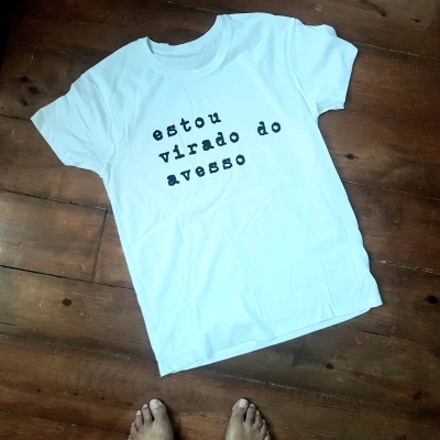 T-shirt branca com texto em preto sobre chão de madeira