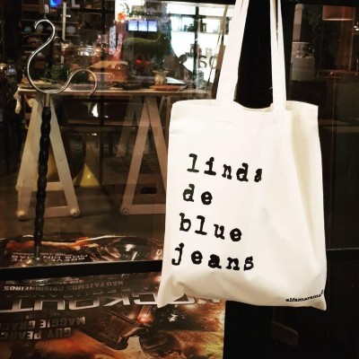 Mala tote branca com texto preto pendurada numa maçaneta de porta