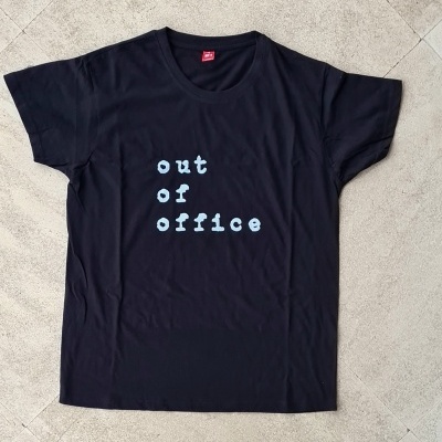 T-shirt preta com texto branco 'out of office' numa superfície de pedra