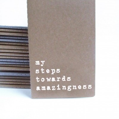 Cadernos marrons com frase 'my steps towards amazingness' na capa