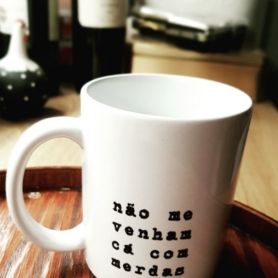 Caneca branca com frase em letras pretas numa bandeja de madeira