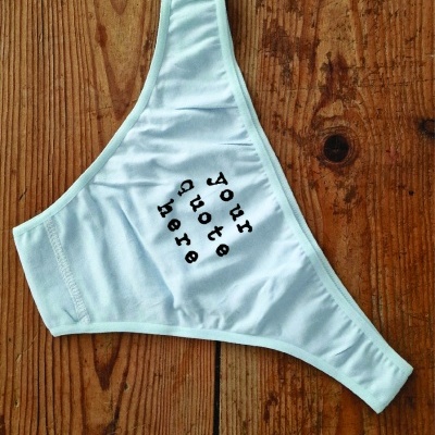 Cueca branca com texto 'your quote here' sobre mesa de madeira