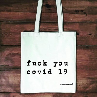 Mala de pano branca com texto preto pendurada numa parede de madeira.