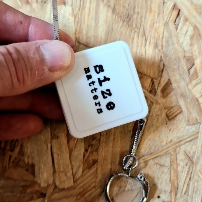 Fita métrica branca com texto '5128 Batteries' e chaveiro sobre madeira