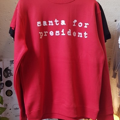 Sweatshirt vermelha com texto branco pendurada em cabide numa loja