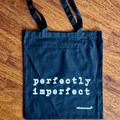Saco de tecido preto com texto branco 'perfectly imperfect'