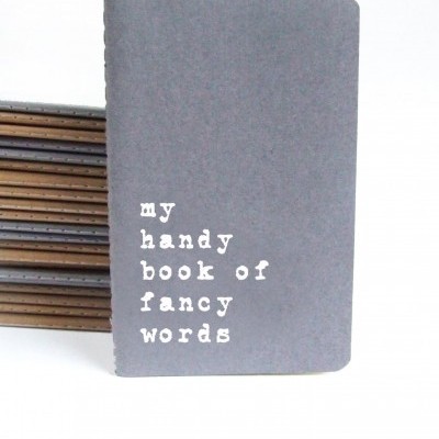 Caderno cinzento com texto branco 'my handy book of fancy words'