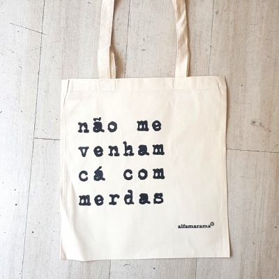 Saco de tecido creme com texto em preto 'não me venham cá com merdas' e marca 'alfamarama'