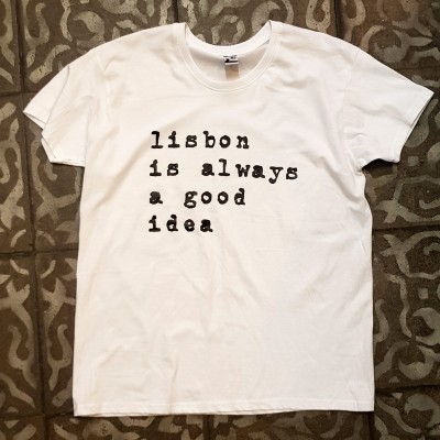 T-shirt branca com texto preto 'lisbon is always a good idea' sobre chão com padrão geométrico