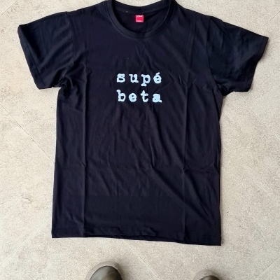 T-shirt preta com texto branco supé beta no centro sobre piso de cimento claro