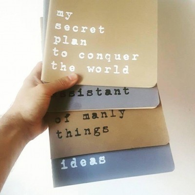 Cadernos coloridos com textos em letras minúsculas, segurados por uma mão sobre fundo branco