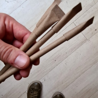 Pessoa segurando três pincéis de maquilhagem com cabos castanhos