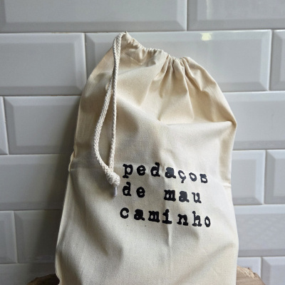 Saco de algodão cru com texto pedaços de mau caminho em fundo de azulejos brancos tipo metro