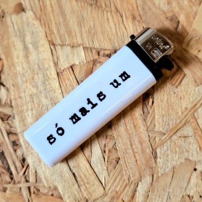 Isqueiro branco com texto 'só mais um' sobre superfície de madeira