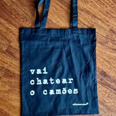 Saco de pano azul escuro com texto branco 'vai chatear o camões'