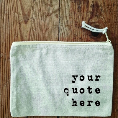 Bolsa de tecido branca com texto e fecho, sobre mesa de madeira