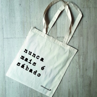 Saco de tecido branco com texto preto 'nunca mais é sábado'