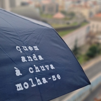 Guarda-chuva azul escuro com mensagem em branco visto em cenário urbano nublado