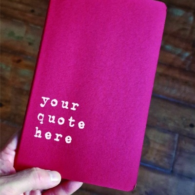 Caderno vermelho com texto branco 'your quote here'