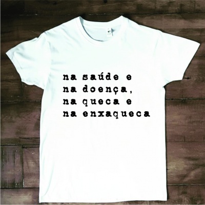 Camiseta branca com texto em português sobre fundo de madeira escura.