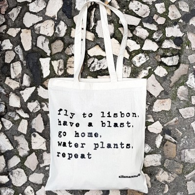 Saco de tecido branco com texto em preto sobre calçada portuguesa