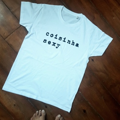 T-shirt branca com texto 'coisinha sexy' em preto sobre chão de madeira escura
