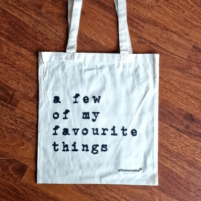 Saco de pano branco com texto preto sobre chão de madeira escura.