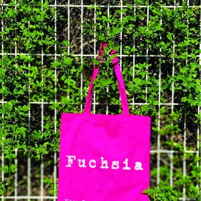 Saco de tecido fúcsia com texto impresso pendurado em vedação com folhagem verde