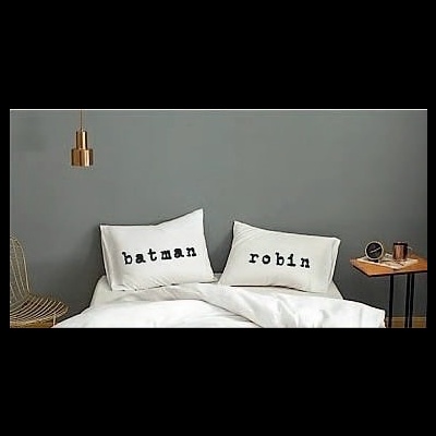 Cama com almofadas 'batman' e 'robin' e mesa de cabeceira com adornos