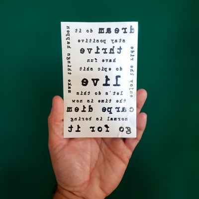 Placa branca com texto espelhado em várias fontes a ser segurada por uma mão contra fundo verde