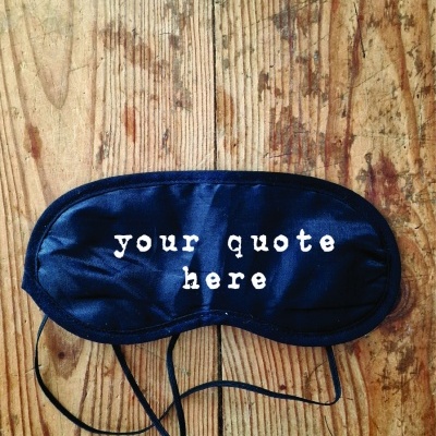 Máscara de sono preta com texto 'your quote here' sobre madeira