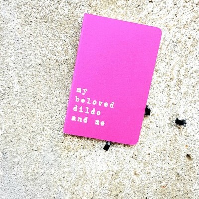 Caderno cor-de-rosa com texto branco na capa sobre parede clara texturizada