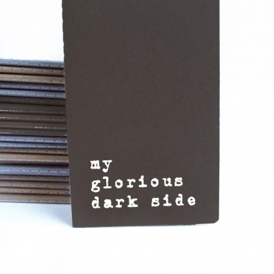 Caderno preto com texto branco 'my glorious dark side'