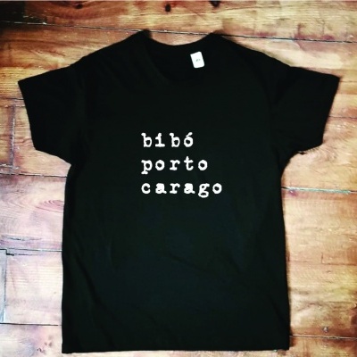 T-shirt preta com texto branco 'bibó porto carago' em fundo madeira