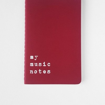 Caderno vermelho com texto branco 'my music notes' em fundo branco