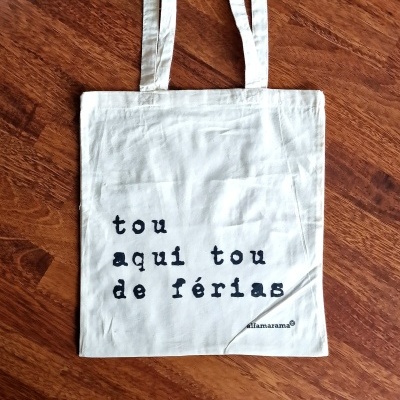 Saco de tecido branco com texto preto pendurado em chão de madeira castanha