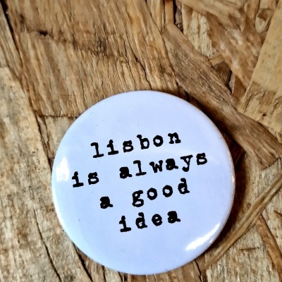 Botão branco com texto Lisboa is always a good idea sobre madeira rústica