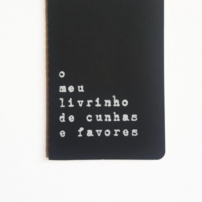 Caderno preto com texto branco 'o meu livrinho de cunhas e favores'