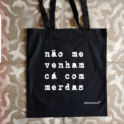 Sacola preta de tecido com texto branco impresso e padrão geométrico no chão