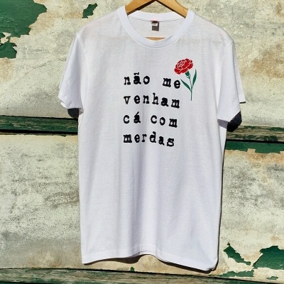 T-shirt branca com texto em português e uma flor vermelha pendurada na parede desgastada