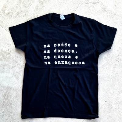 T-shirt preta com texto branco em português sobre um fundo de pedra clara.