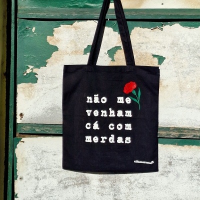 Saco preto com texto branco e flor vermelha pendurado numa porta de madeira verde desgastada