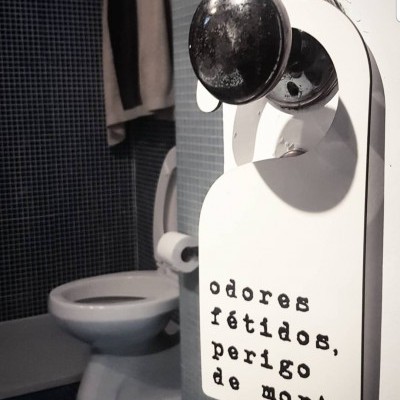 Cabide de porta com aviso em casa de banho, com texto 'odores fétidos, perigo de morte'.