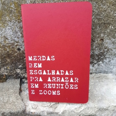 Caderno vermelho com texto branco sobre reuniões, apoiado em parede de pedra