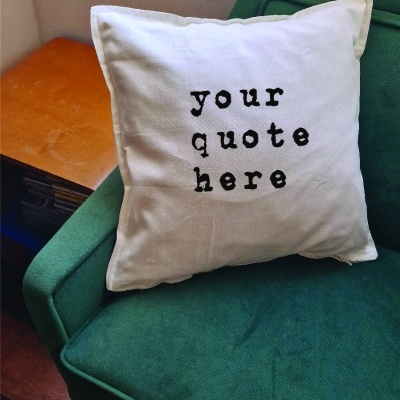 Almofada branca com texto preto sobre poltrona verde junto a janela