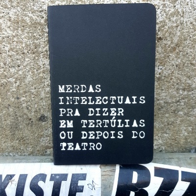 Caderno preto com texto branco apoiado numa superfície frente a uma parede texturada