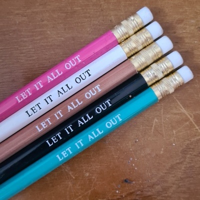 Cinco lápis de madeira coloridos com texto LET IT ALL OUT dispostos sobre madeira