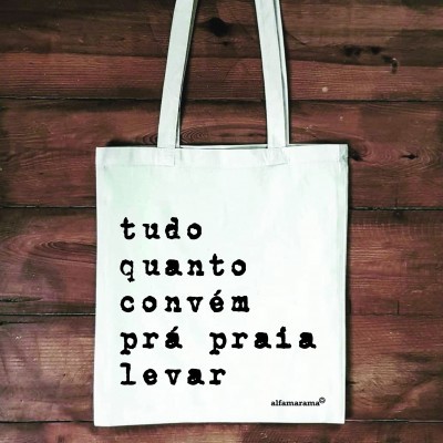 Mala tote branca com texto preto pendurada numa parede de madeira