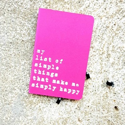 Caderno rosa com texto branco sobre uma parede bege texturada