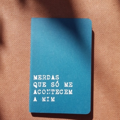 Caderno azul com texto branco na capa sobre tecido cor de terra